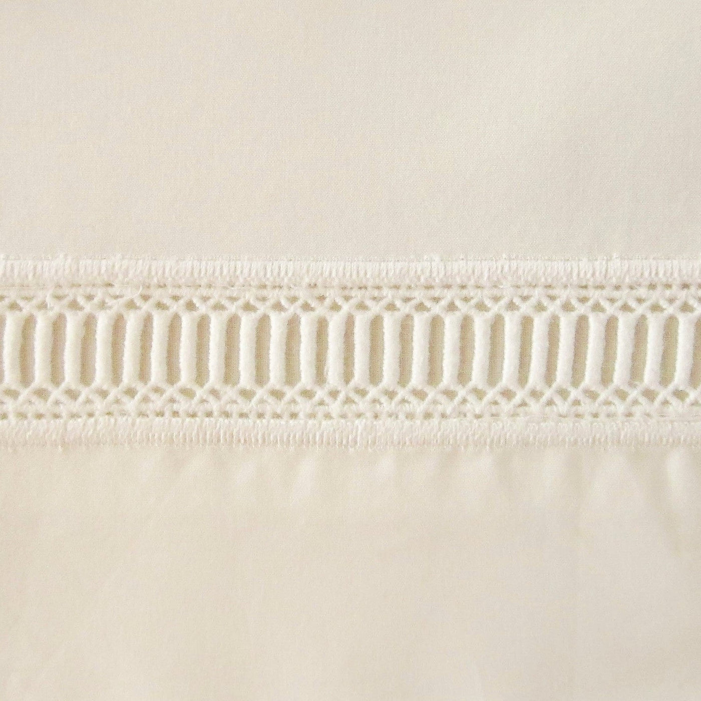 Close-up of ivory cotton fabric with geometric openwork lace trim detail.