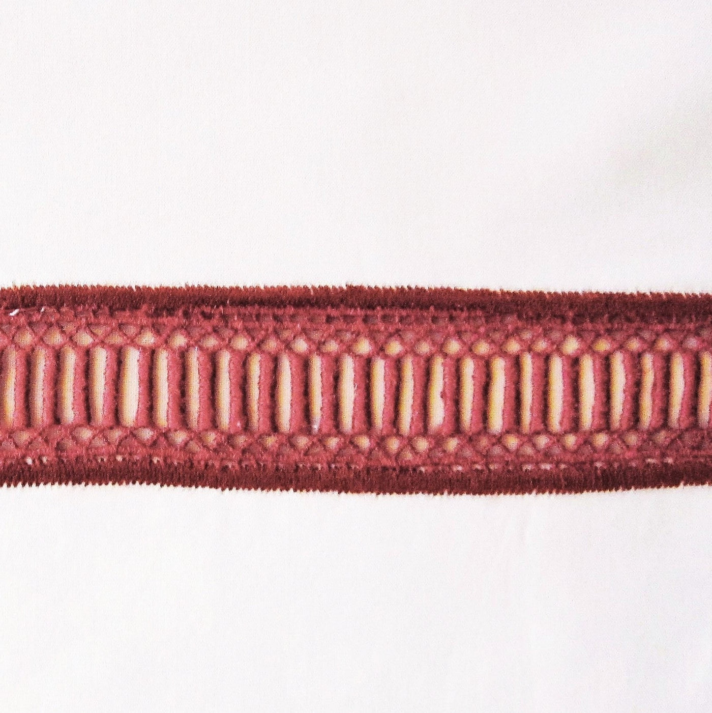 Close-up of Doric burgundy embroidered border trim on white linen fabric.