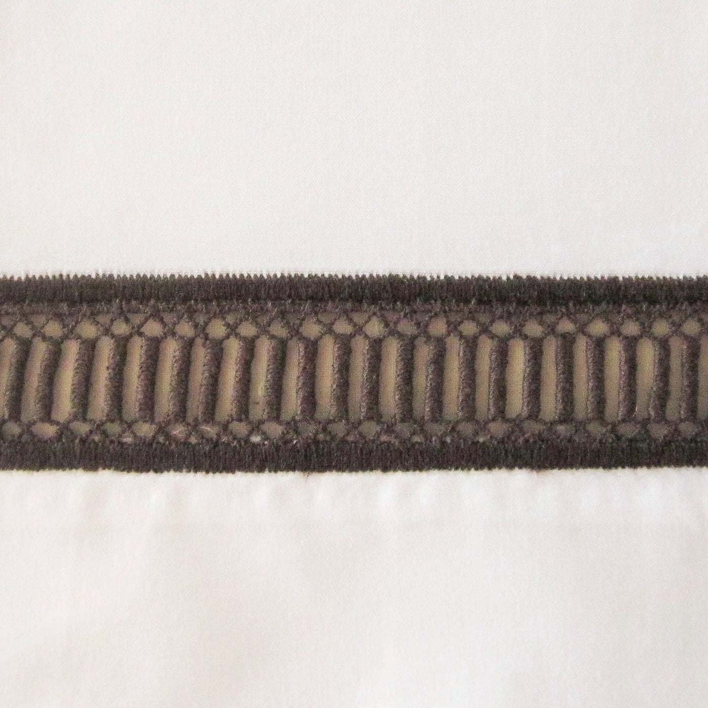 Close-up of Doric dark brown geometric woven trim detail on white linen.