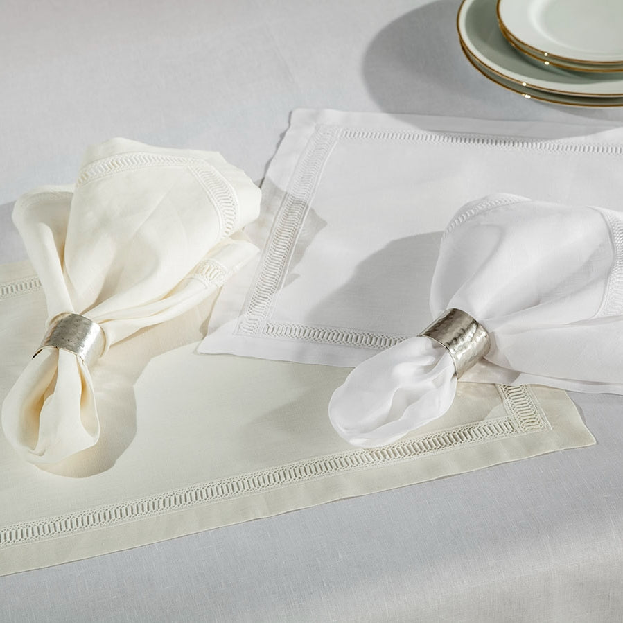 Close-up of ivory and white linen napkins with hemstitch borders, styled with silver napkin rings.