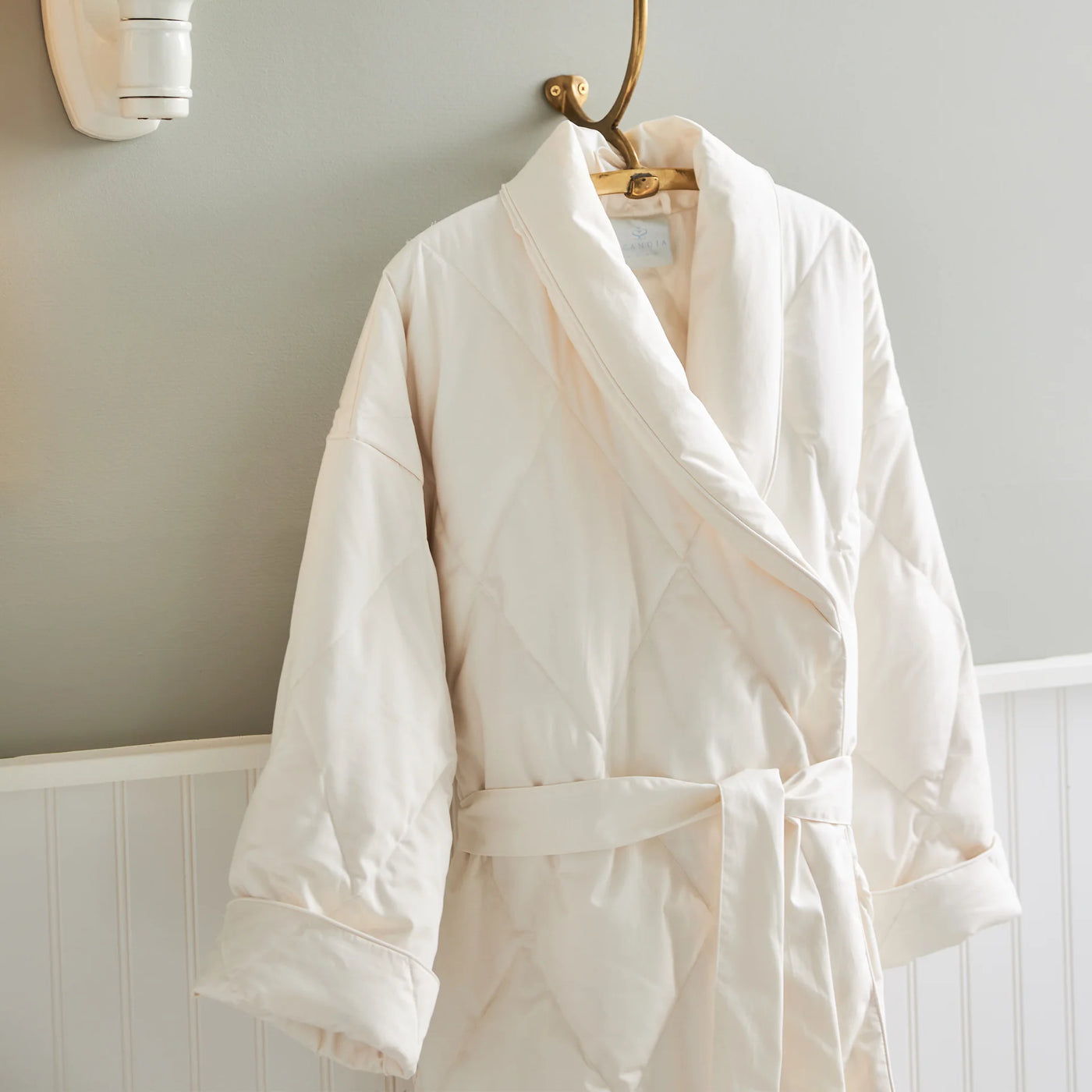 Scandia Home ivory quilted down robe with shawl collar hung on brass hook.