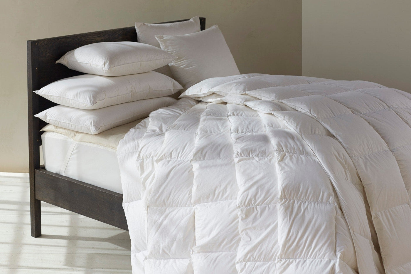 Ivory down comforter draped over bed with matching pillow inserts on dark wood headboard.