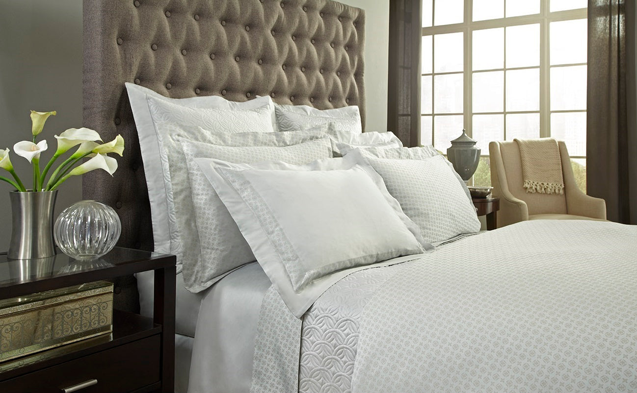 White Home Treasures Duomo bedding styled on bed with tufted grey upholstered headboard.
