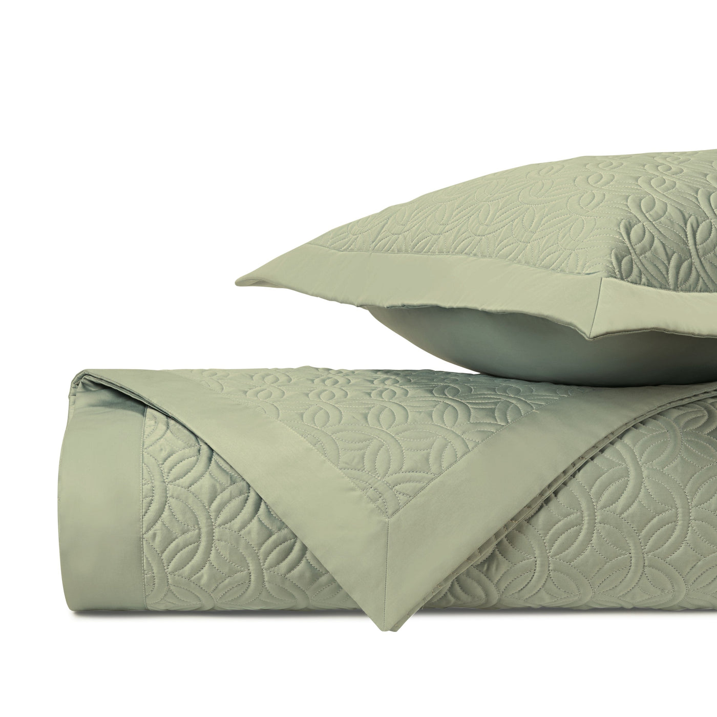 Sage green quilted coverlet folded beside a matching sham, showing geometric pattern detail.