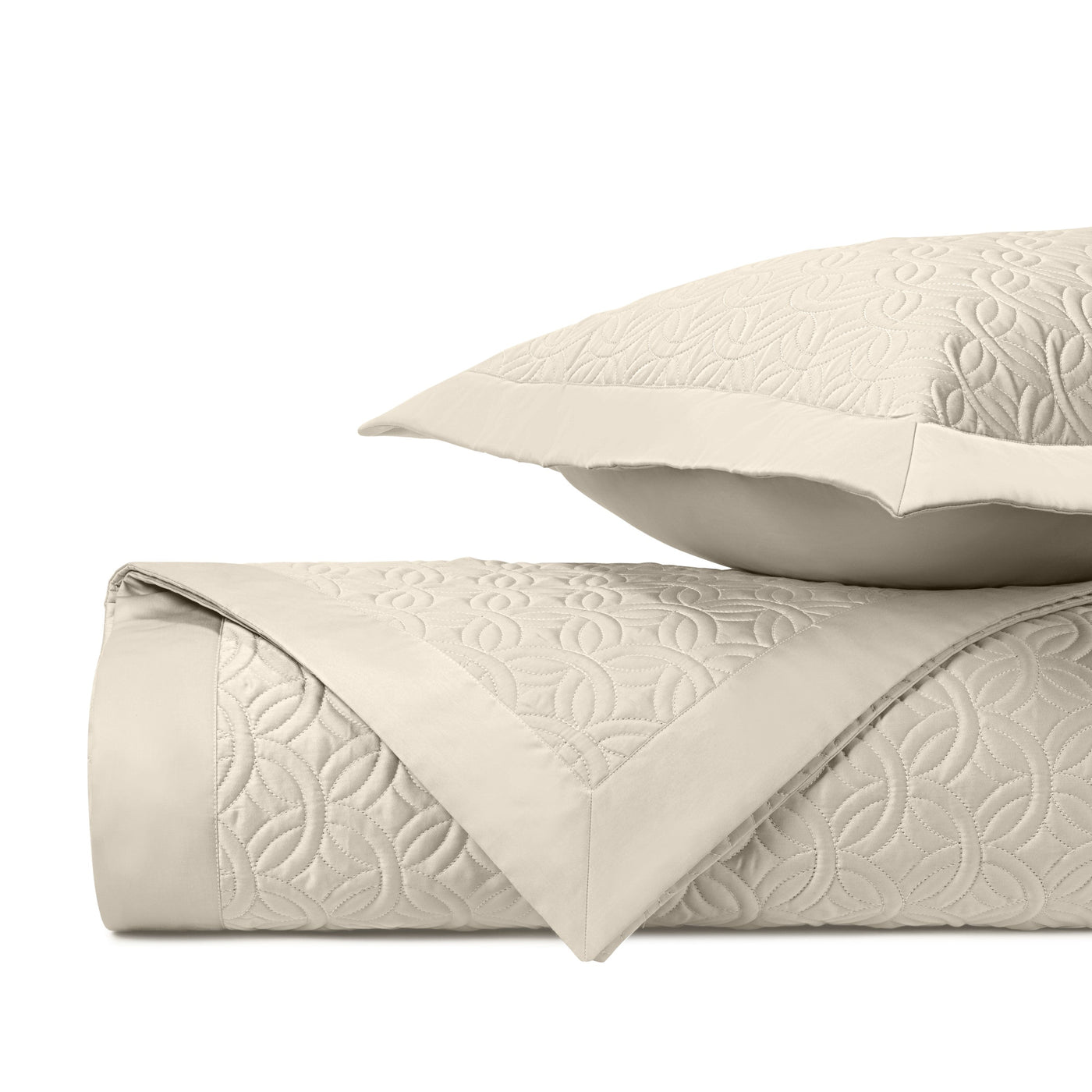 Close-up of ivory quilted coverlet and sham showing geometric floral matelassé pattern.