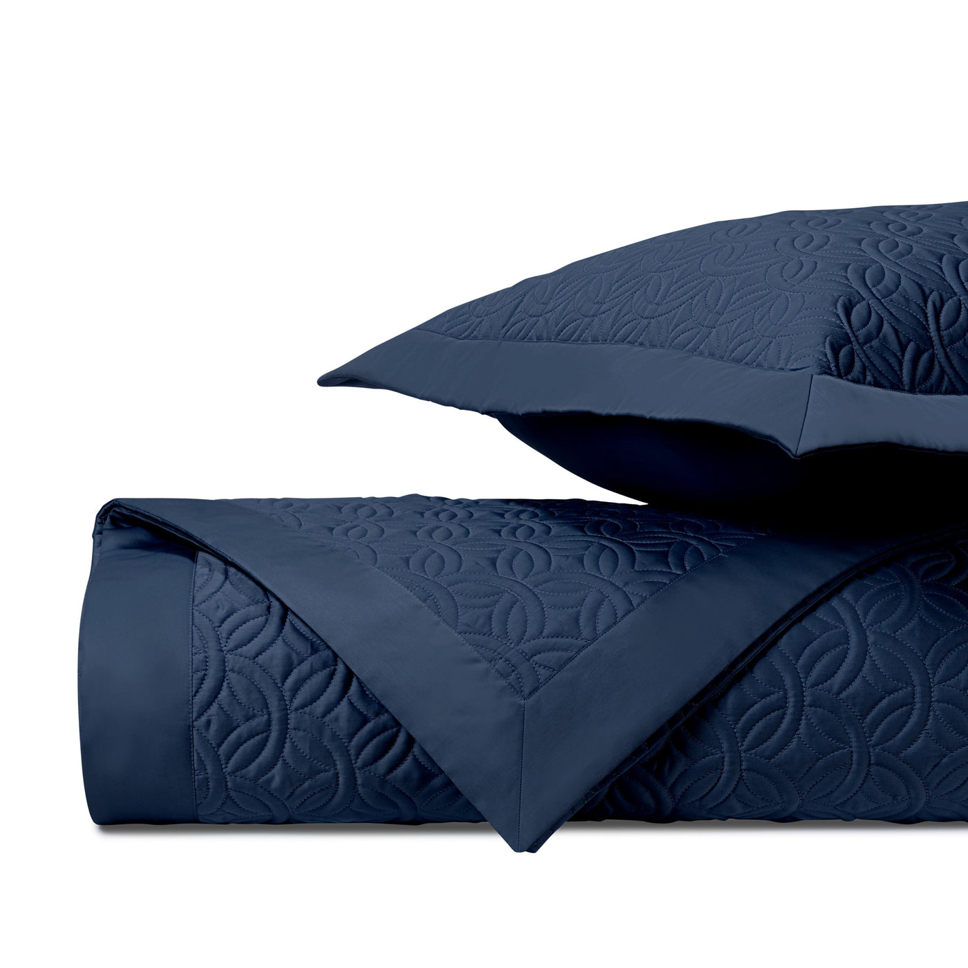 Close-up of navy Duomo quilted coverlet showing geometric medallion stitch pattern and folded edge.