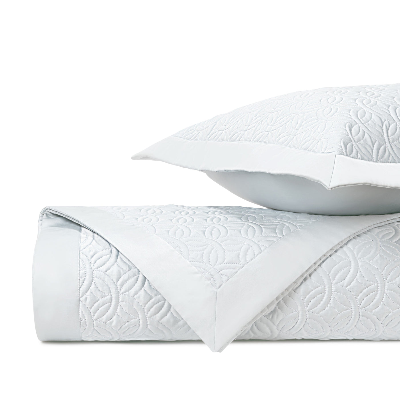 Close-up of quilted white coverlet and sham showing embossed floral geometric pattern.