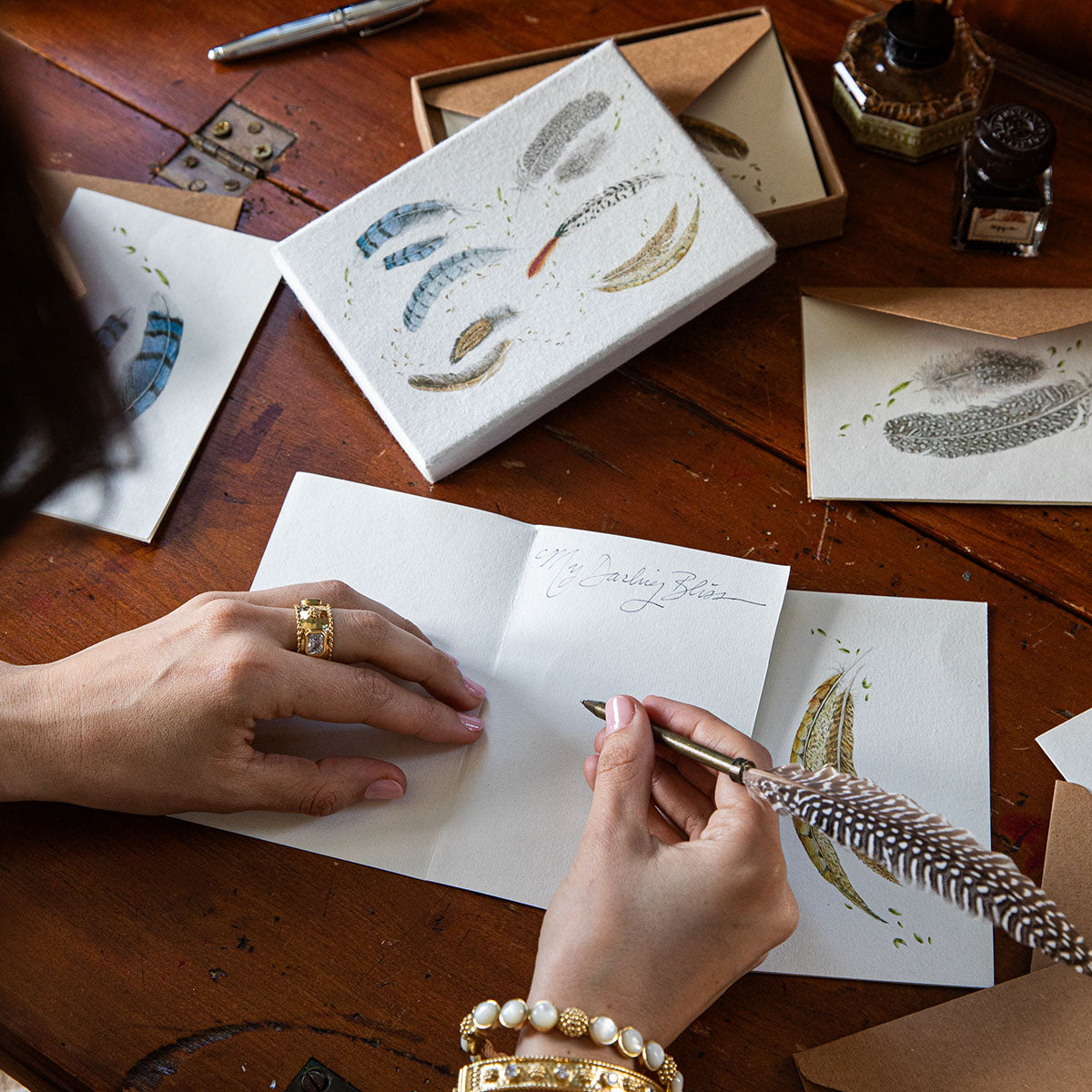 Hand writing with a feather quill in a Forest Walk note card on a wooden desk