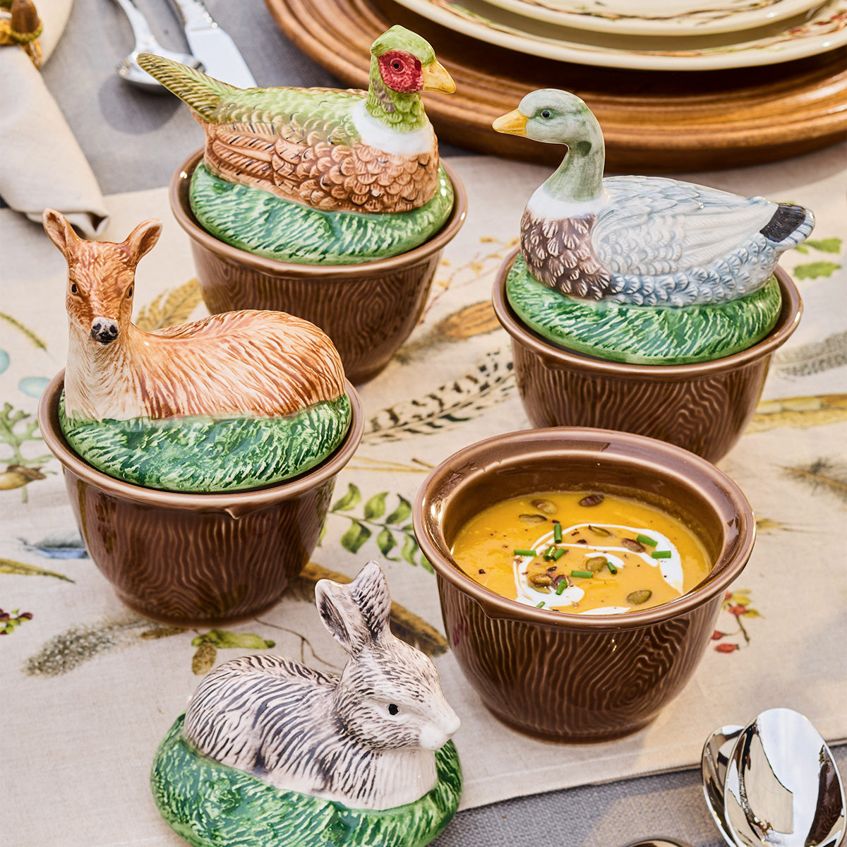 Forest Walk rabbit, pheasant, deer and duck lidded bowls on a table, one open bowl holding soup