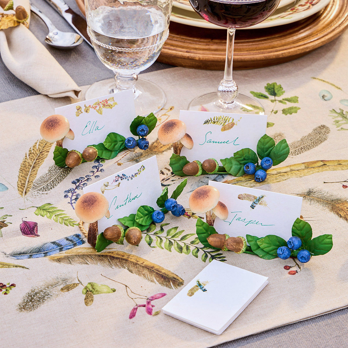 Forest Walk place cards in mushroom and acorn holders on a feather print tablecloth