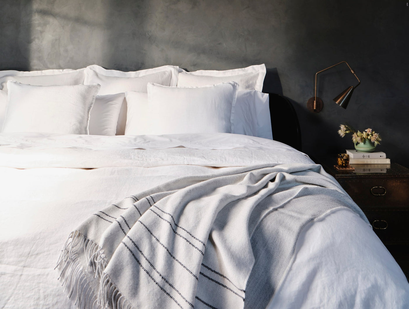 White alpaca throw with charcoal stripes and fringe draped over a bed in a moody dark room.