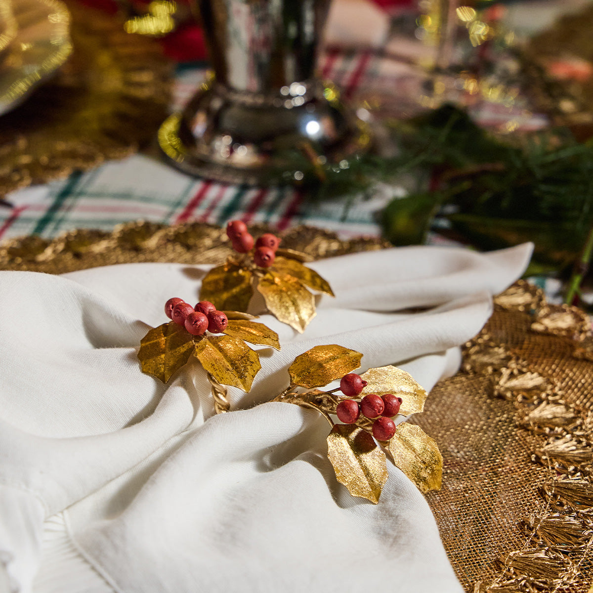 Close-up of gold holly napkin rings with red berries on white napkins on a gold charger