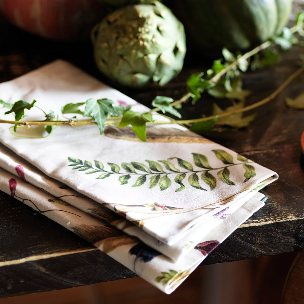 Forest Walk cotton napkins folded on a wood table beside an artichoke and greenery