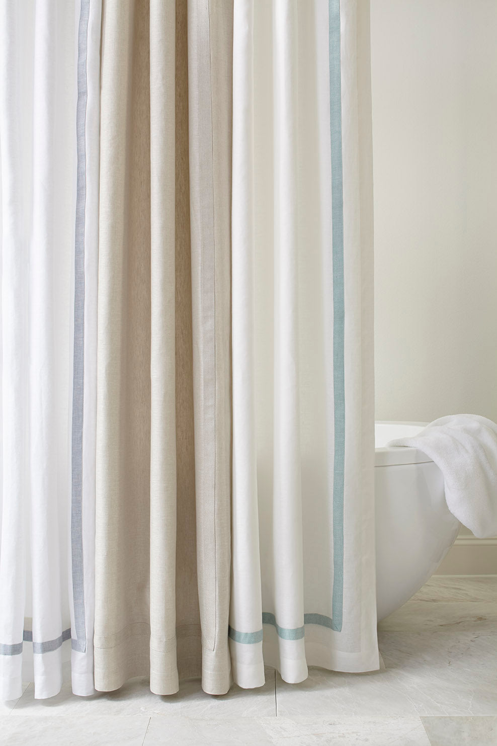 Three Fino shower curtains in ivory linen with contrast border trim in slate, sand, and spa blue.