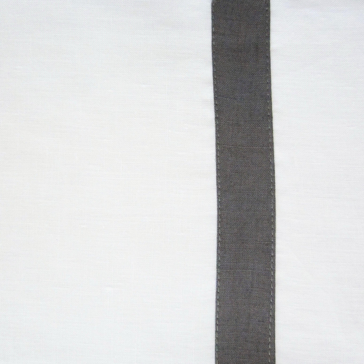 Close-up of charcoal linen border with topstitching detail on white tablecloth.