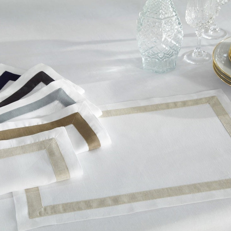 Fino placemats fanned in navy, black, grey, taupe, and white with mitered border trim.