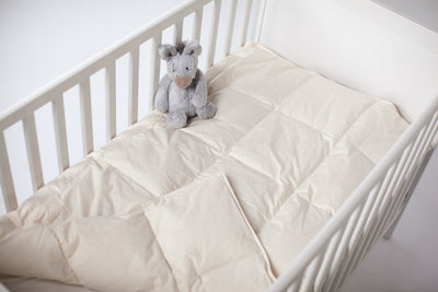 Ogallala Comfort Fiona Hypodown ivory crib comforter in white crib with stuffed animal.