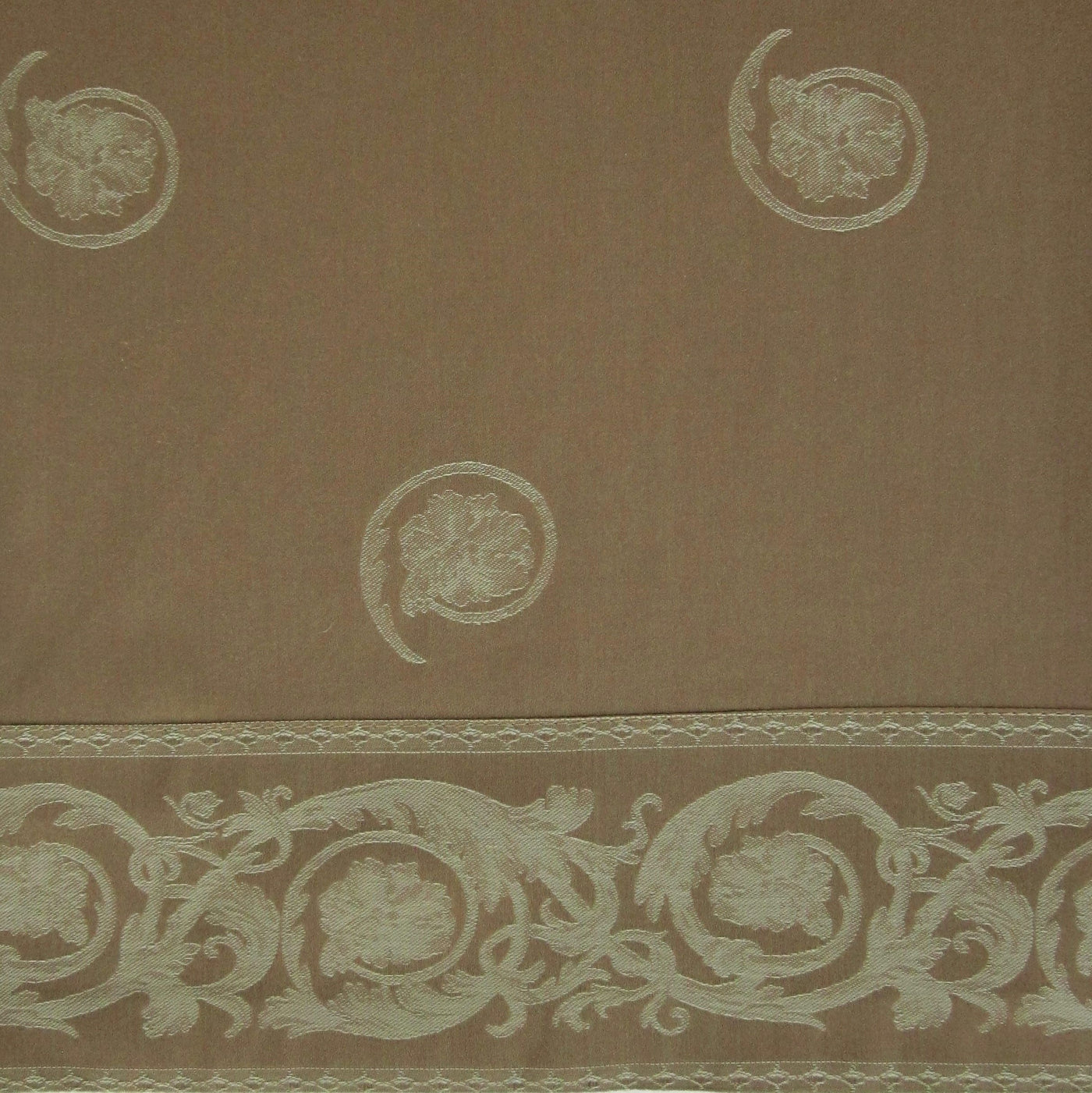Close-up of taupe cotton sham with ivory embroidered medallions and scrolling floral border trim.