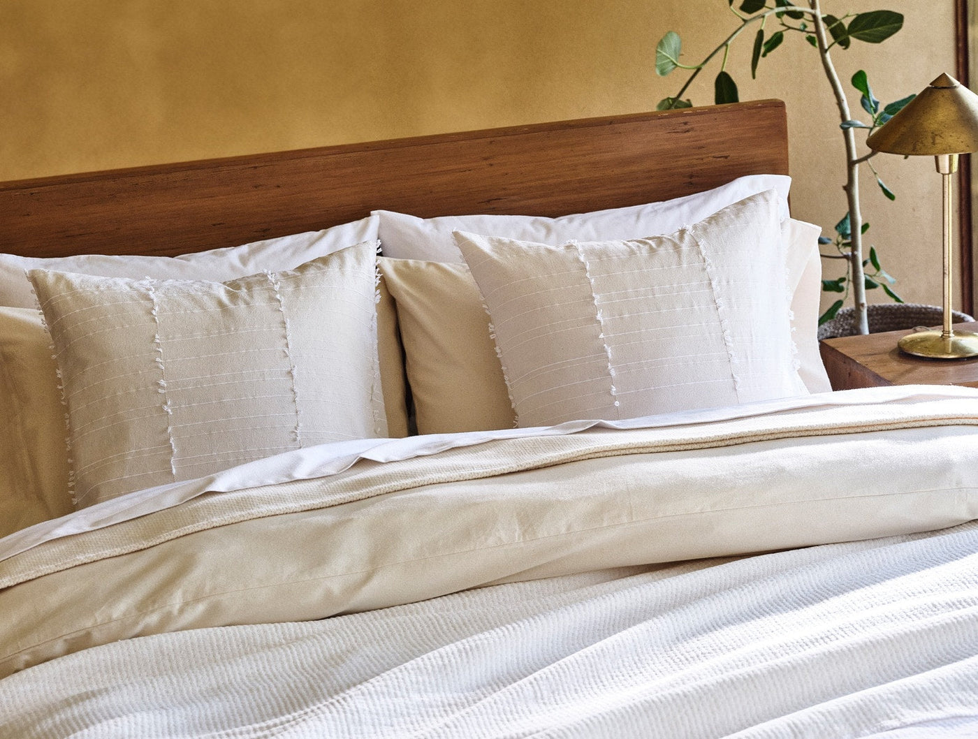 Coyuchi Precita pillow covers in ivory linen with fringe trim, styled on a made bed.