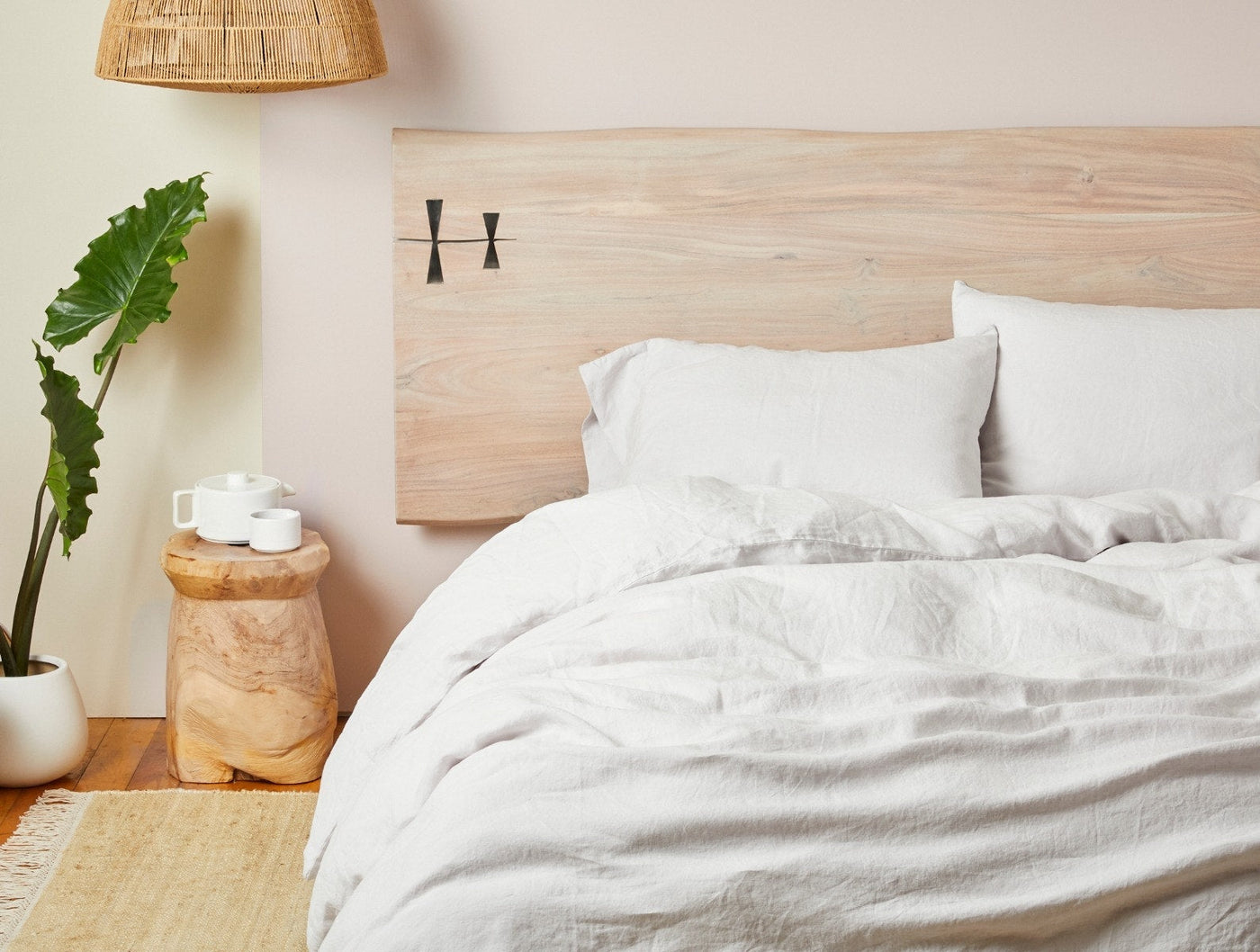 Relaxed Linen sheet set in white styled on bed with natural wood headboard.