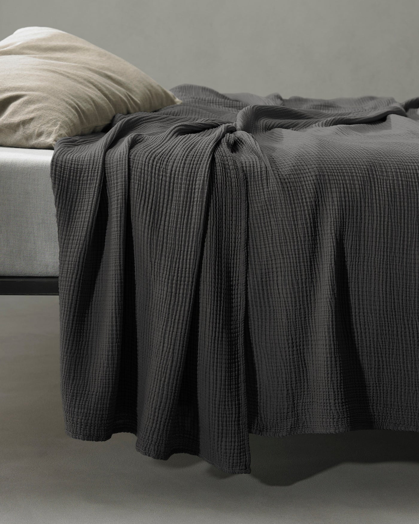 Charcoal waffle-weave coverlet draped over bed edge, showing textured drape and folds.