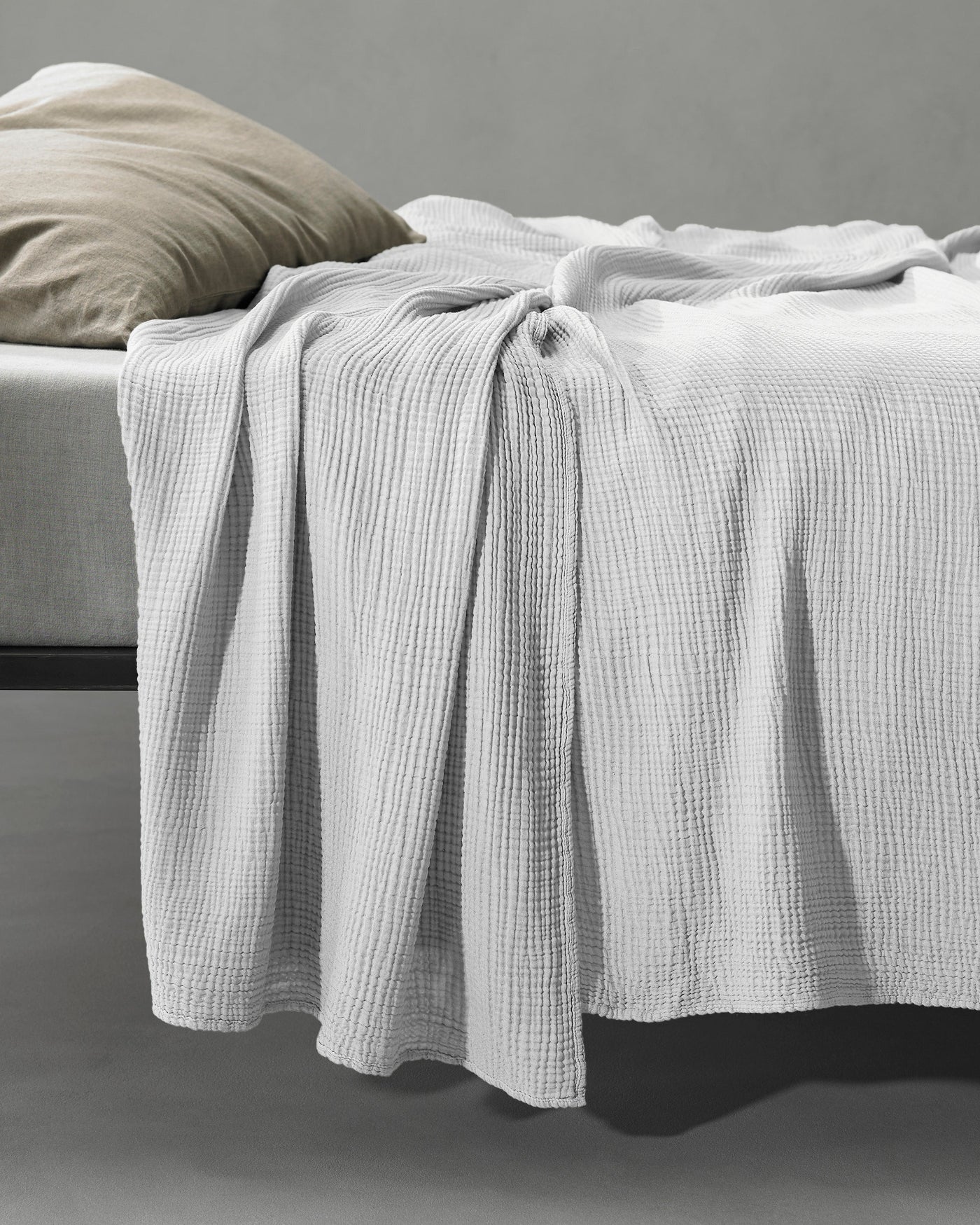 Waffle-weave silver grey coverlet draped over bed foot, cascading to floor.