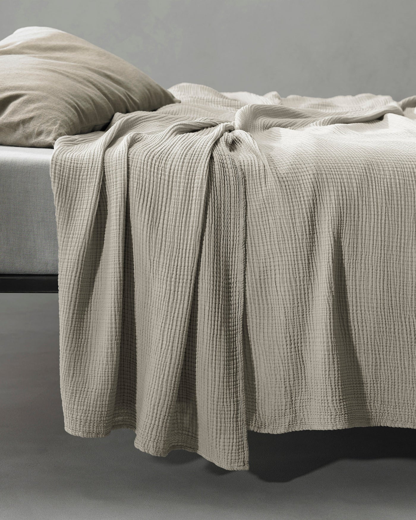 Stone waffle-knit coverlet draped over bed edge, showing textured weave detail.
