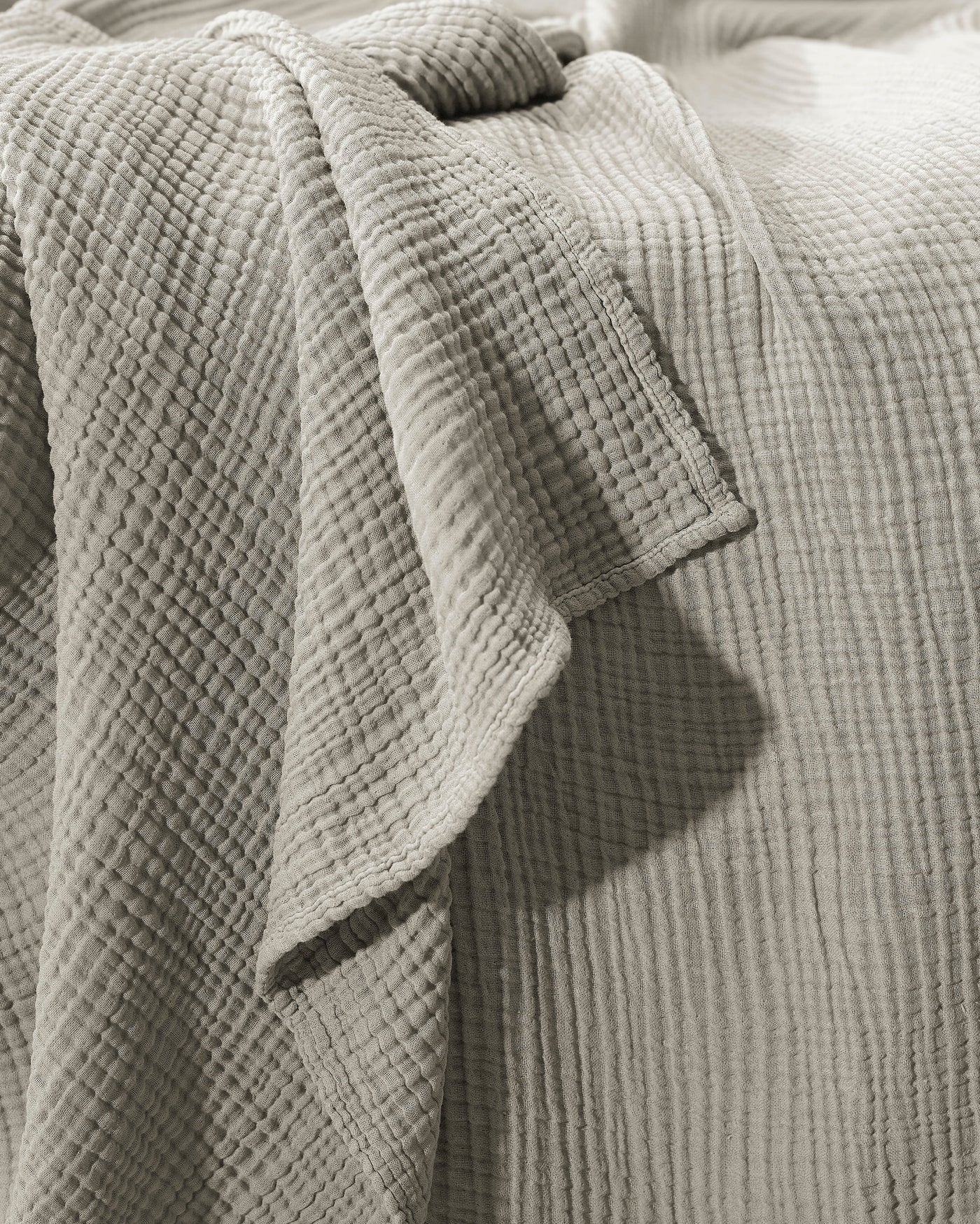 Close-up of sage cotton gauze texture and folded hem detail on a draped coverlet.