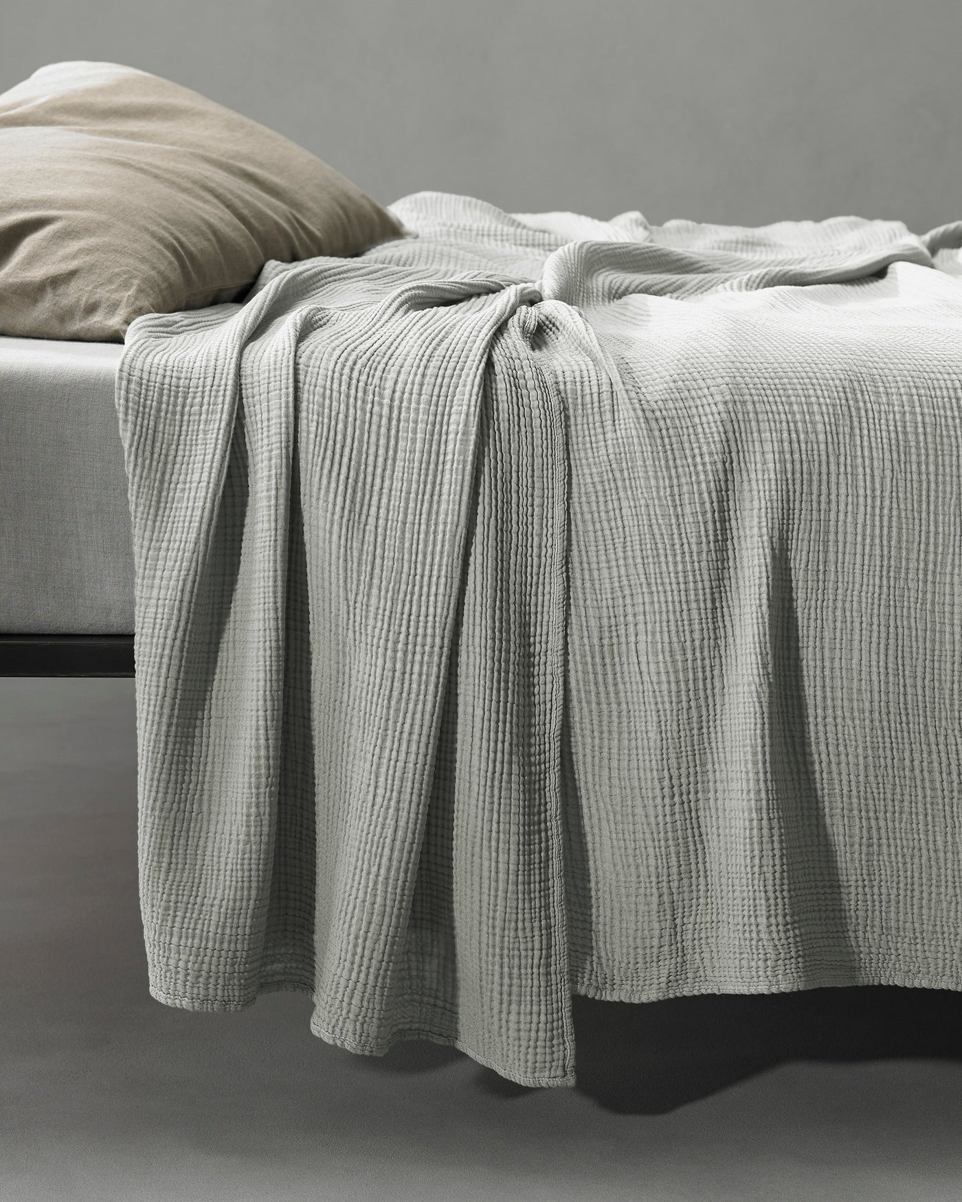 Waffle-textured coverlet in silver grey draped over the edge of a bed.