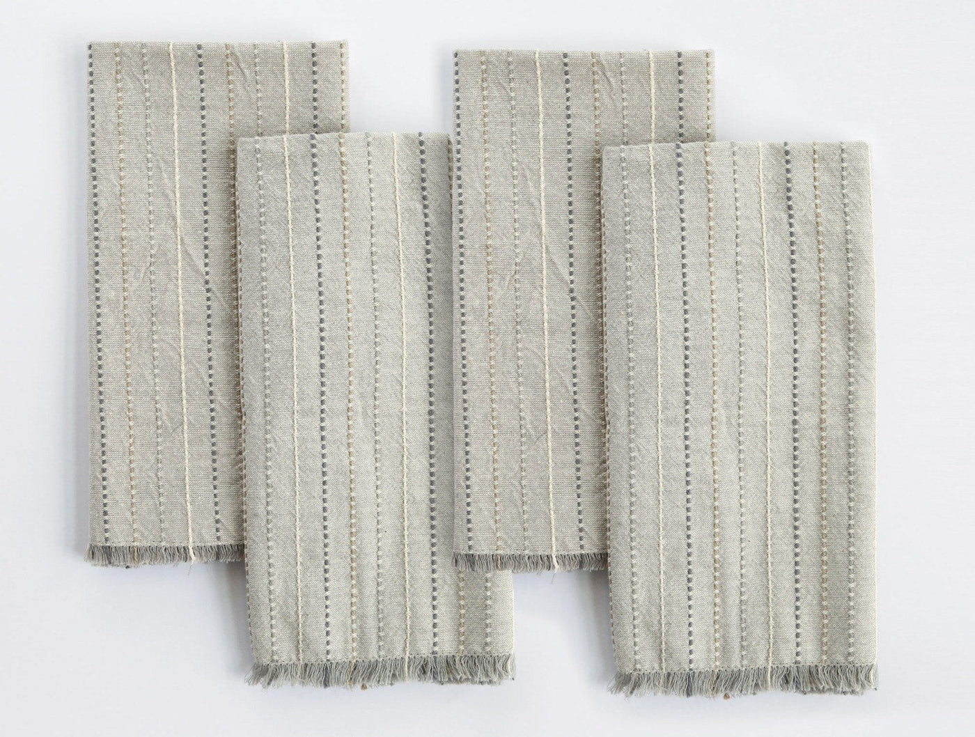 Close-up of four Coyuchi Fringe Stripe napkins in sage, showing dotted stripe weave and frayed hem detail.
