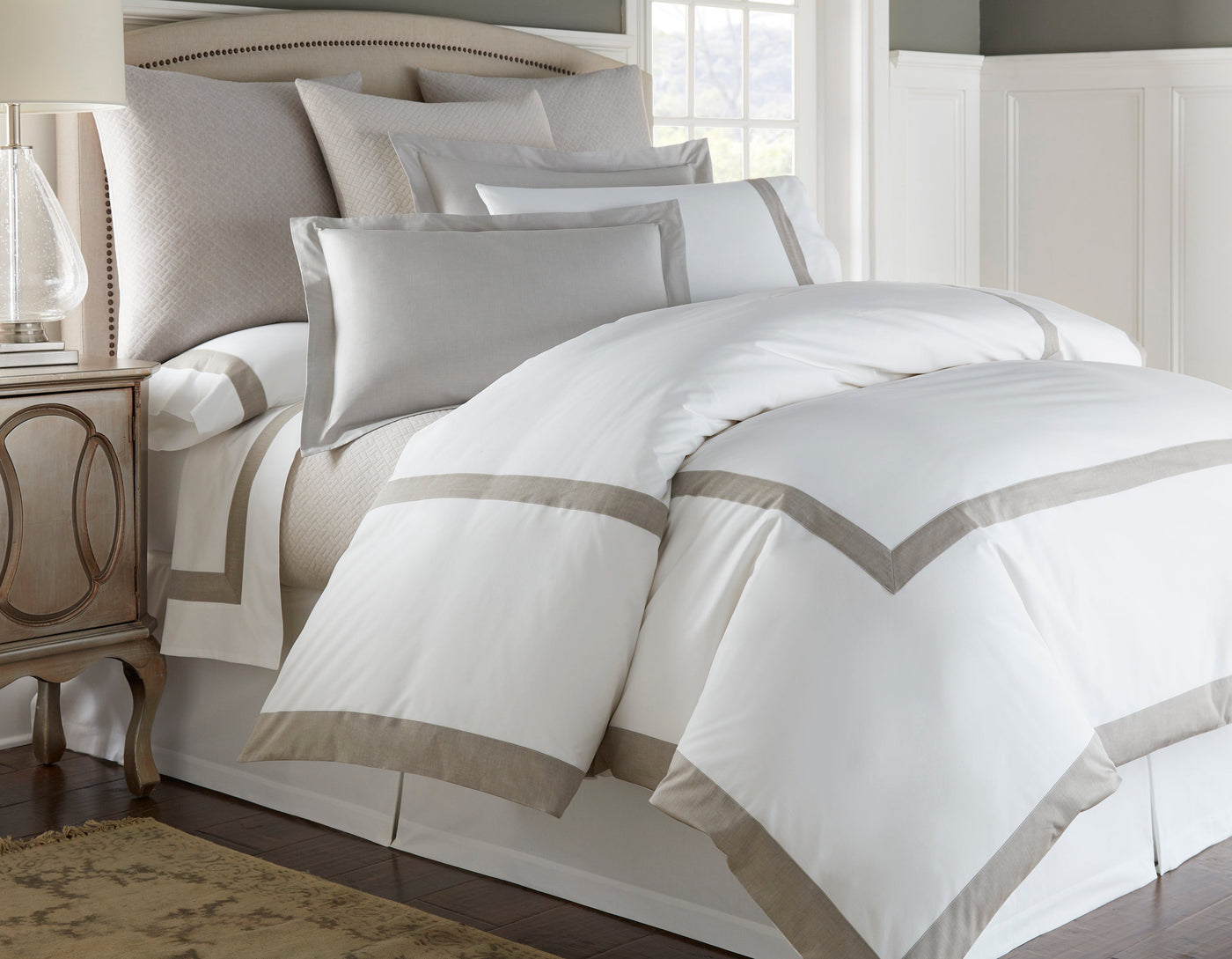White and taupe cotton bedding set with mitered border detail on a styled bed.