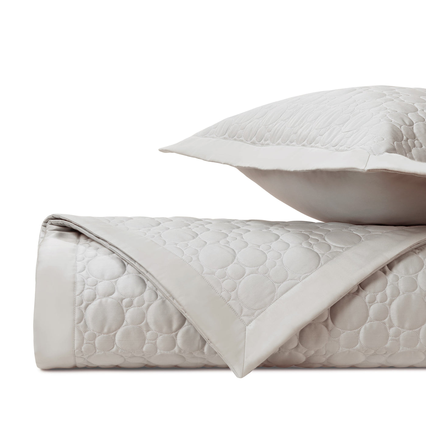 Close-up of ivory quilted fabric with circular medallion pattern and satin border trim.