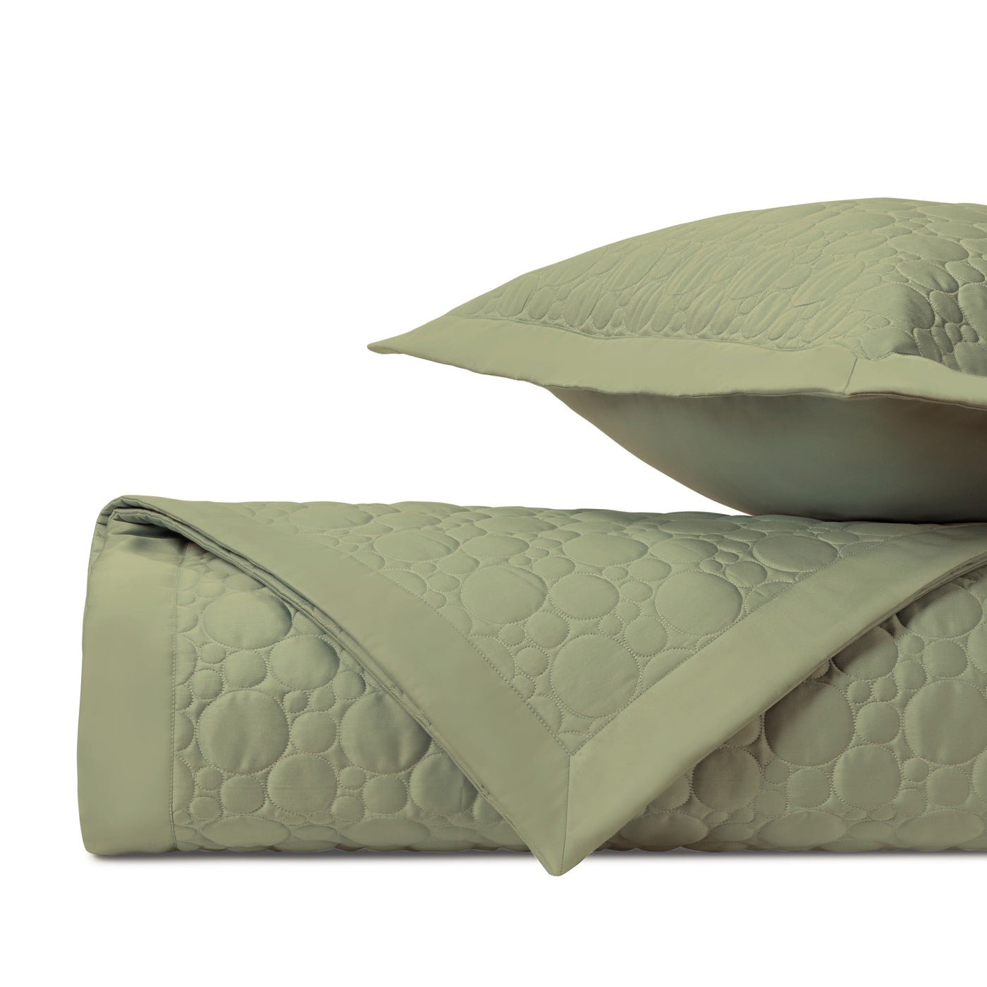 Close-up of sage green quilted coverlet showing circle pattern stitching and folded edge detail.