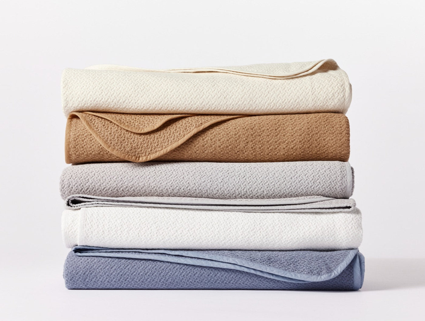 Stack of four folded Coyuchi Honeycomb blankets in ivory, camel, silver, and slate blue.
