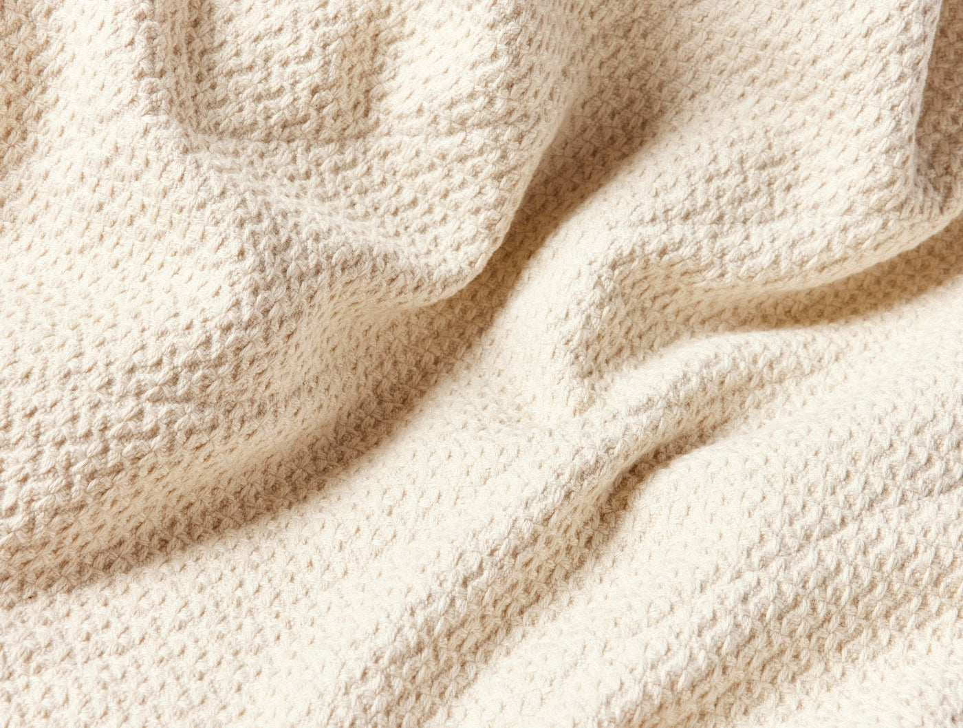 Close-up of ivory Coyuchi Honeycomb blanket showing textured waffle weave and soft drape.