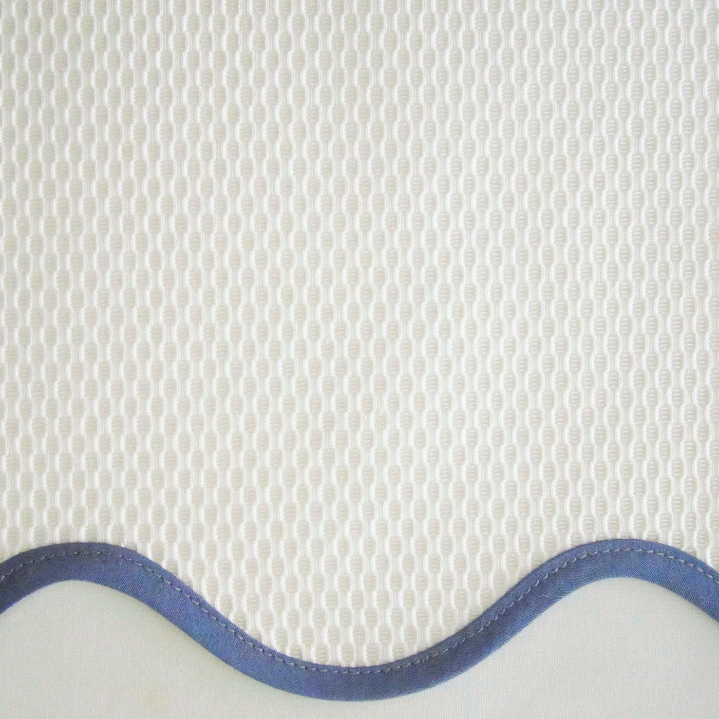 Close-up of ivory honeycomb-weave fabric with a scalloped periwinkle satin trim edge.