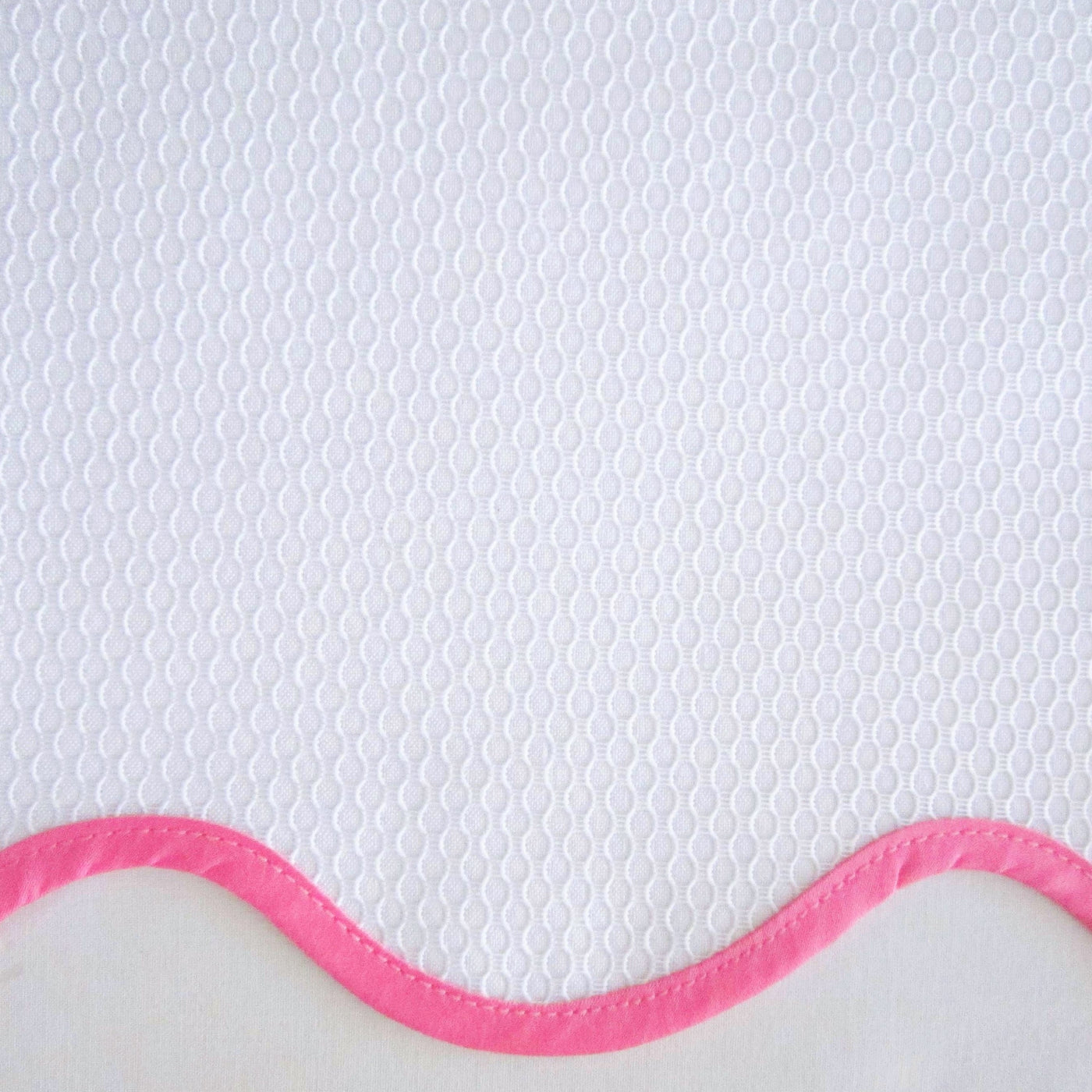 Close-up of white honeycomb-textured fabric with a rose pink scalloped border trim.