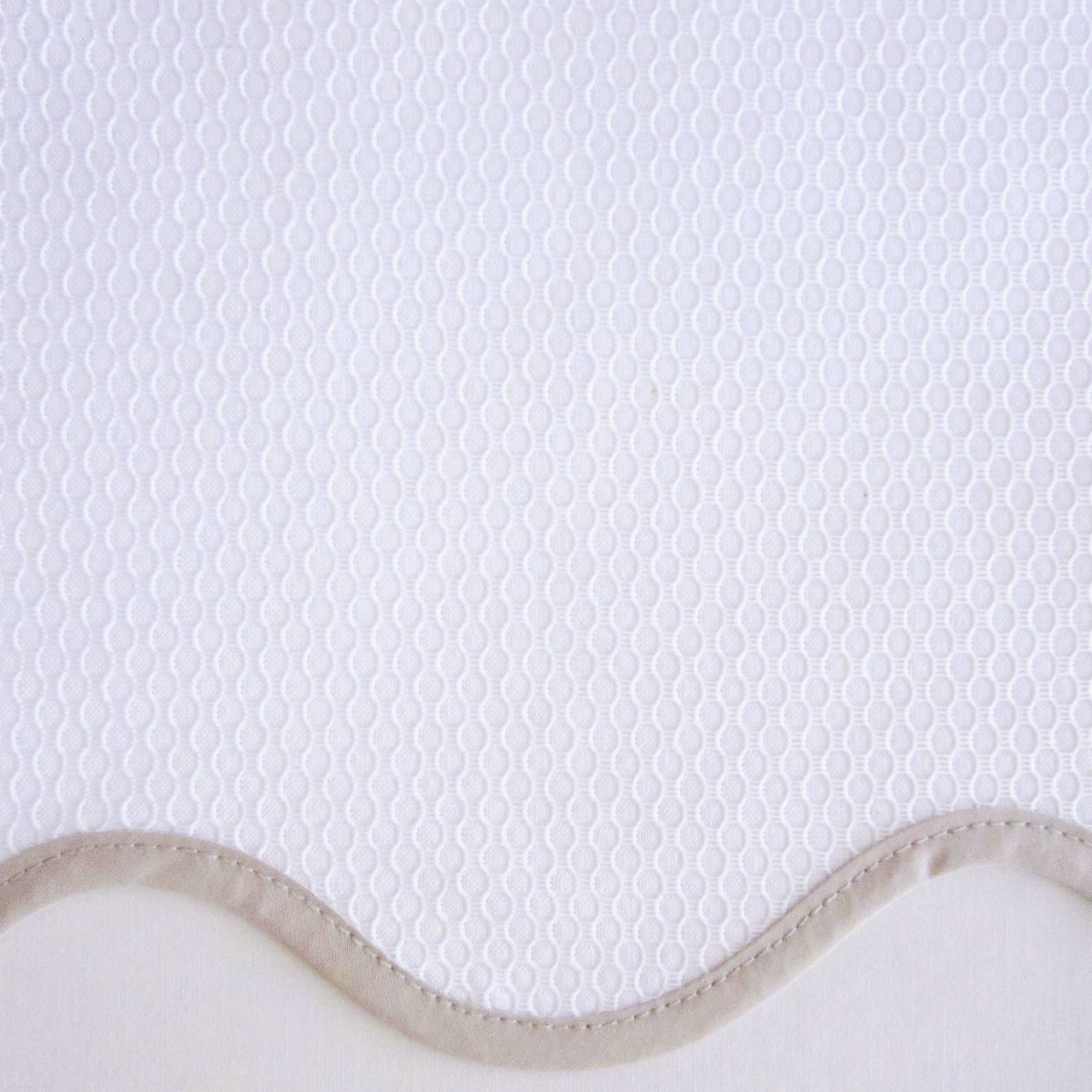 Close-up of white honeycomb-textured fabric with a scalloped edge and taupe border trim.