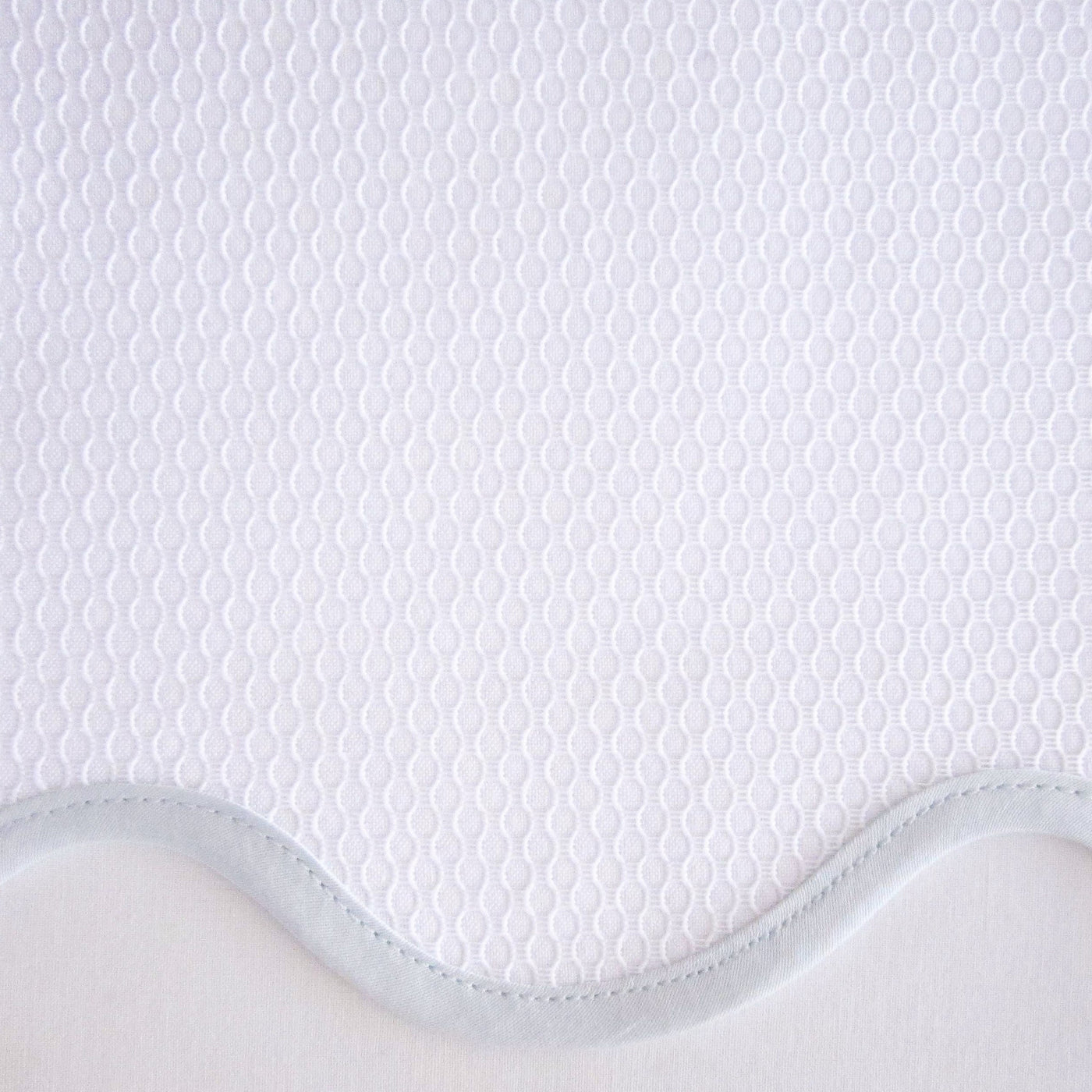 Close-up of white honeycomb-textured fabric with a scalloped edge and pale blue trim.