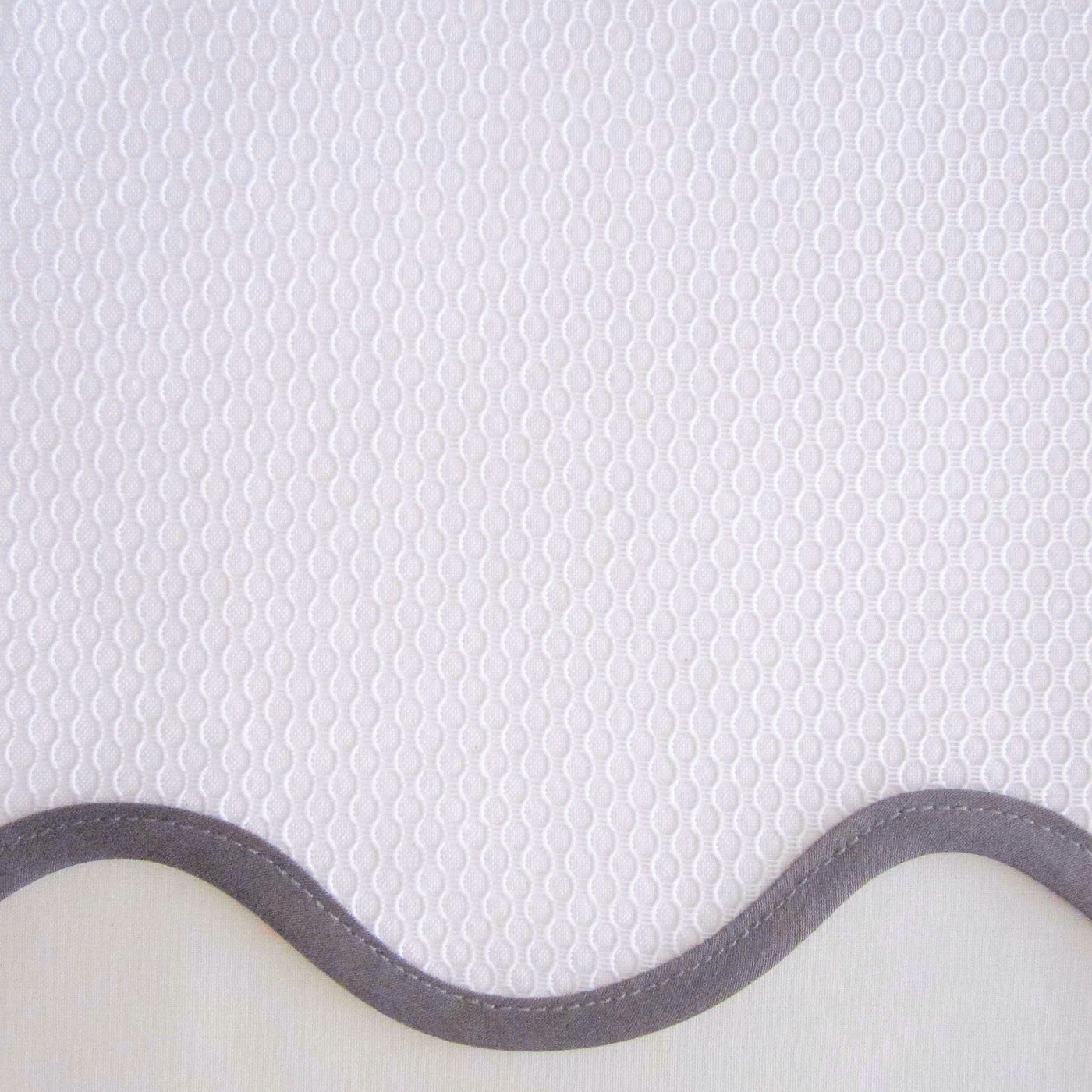 Close-up of white honeycomb-texture fabric with a scalloped grey border edge.