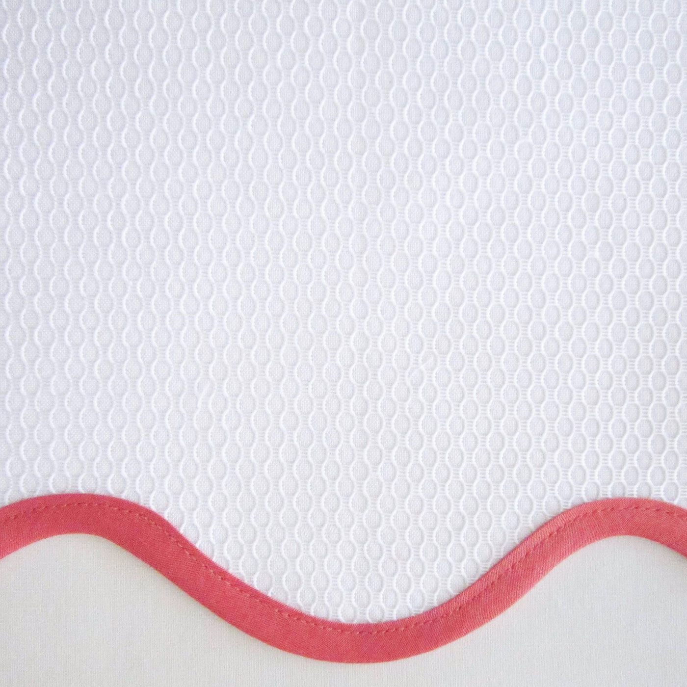 Close-up of white honeycomb-textured fabric with a coral scalloped border edge.
