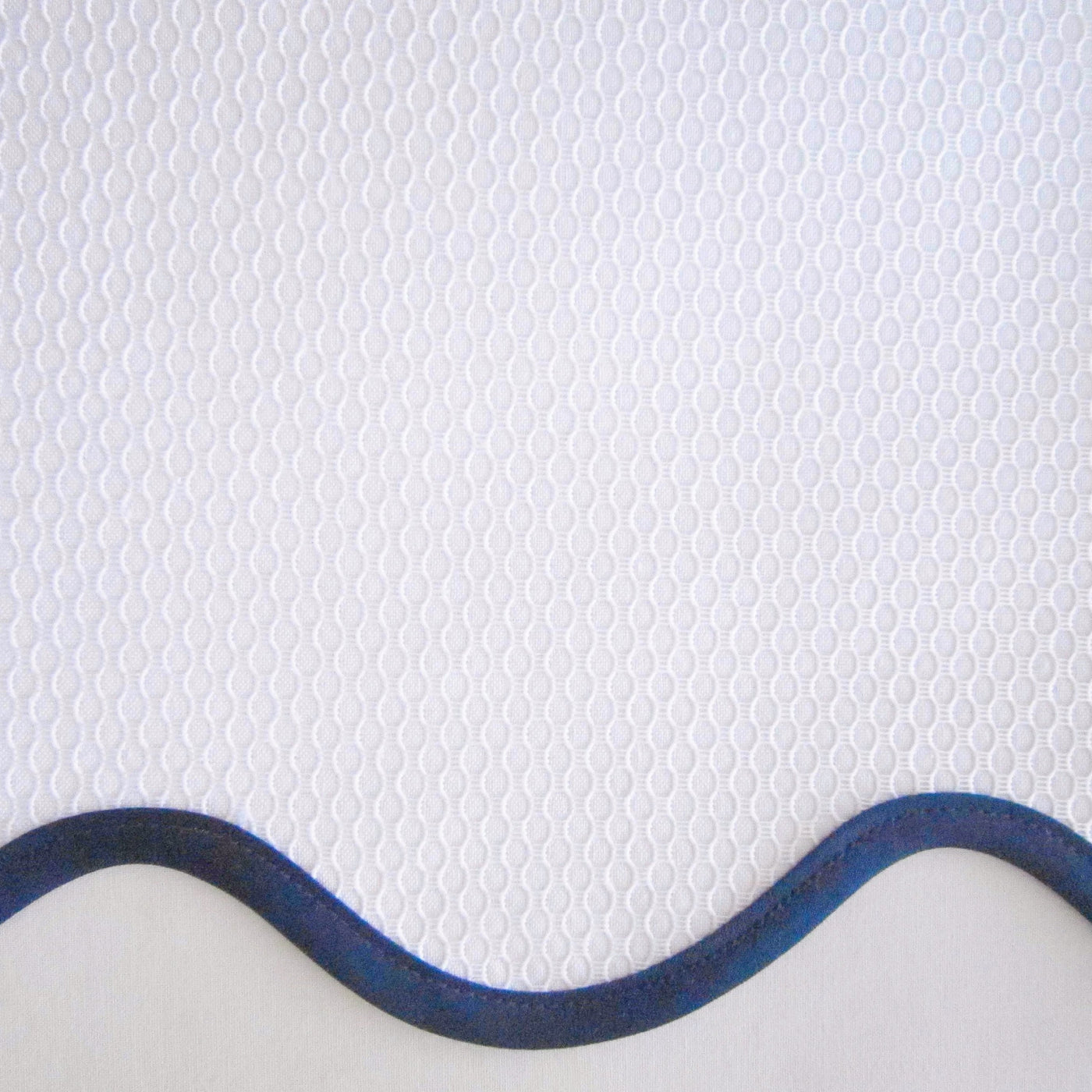 Close-up of white honeycomb-weave fabric with a navy scalloped border edge.
