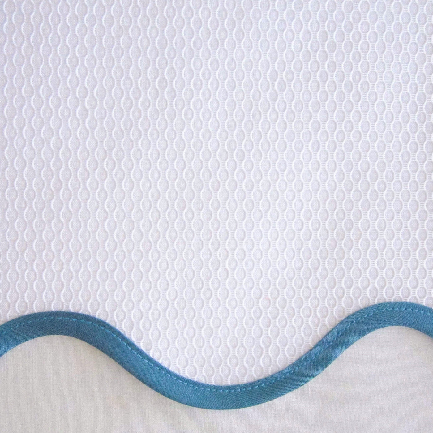 Close-up of white honeycomb-textured fabric with a teal satin trim edge.