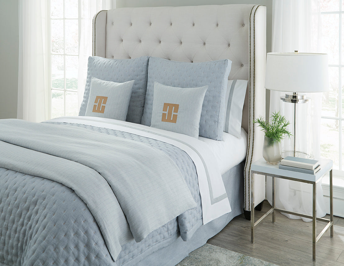 Houston yardage in pale blue styled on a made bed with monogrammed accent pillows.