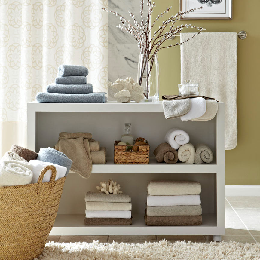 Styled bathroom shelving unit displaying folded and rolled towels in ivory, champagne, and dusty blue.
