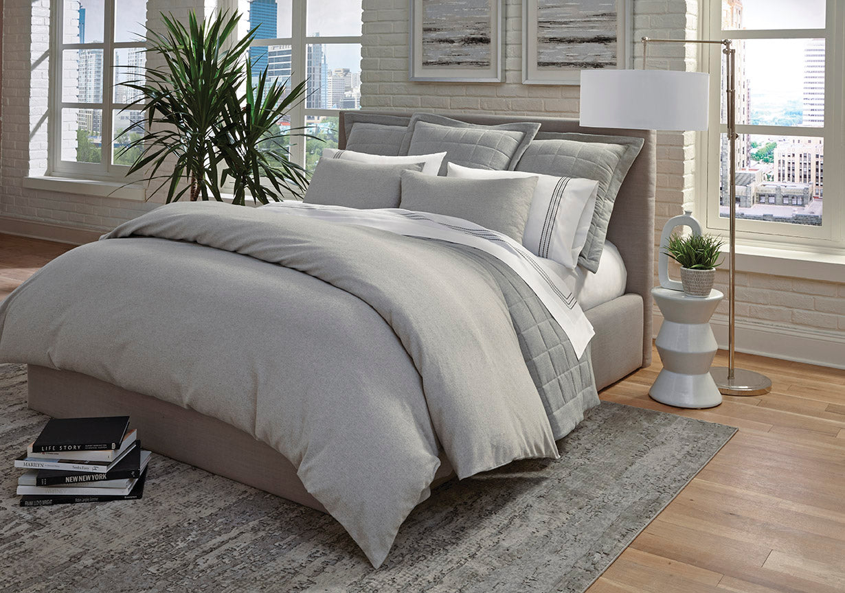 Silver-grey bedding set styled on a modern bed with city view backdrop.