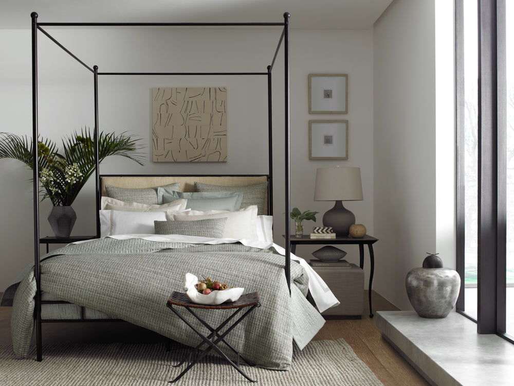 Sage green jacquard bedding styled on a four-poster bed in a serene neutral bedroom.