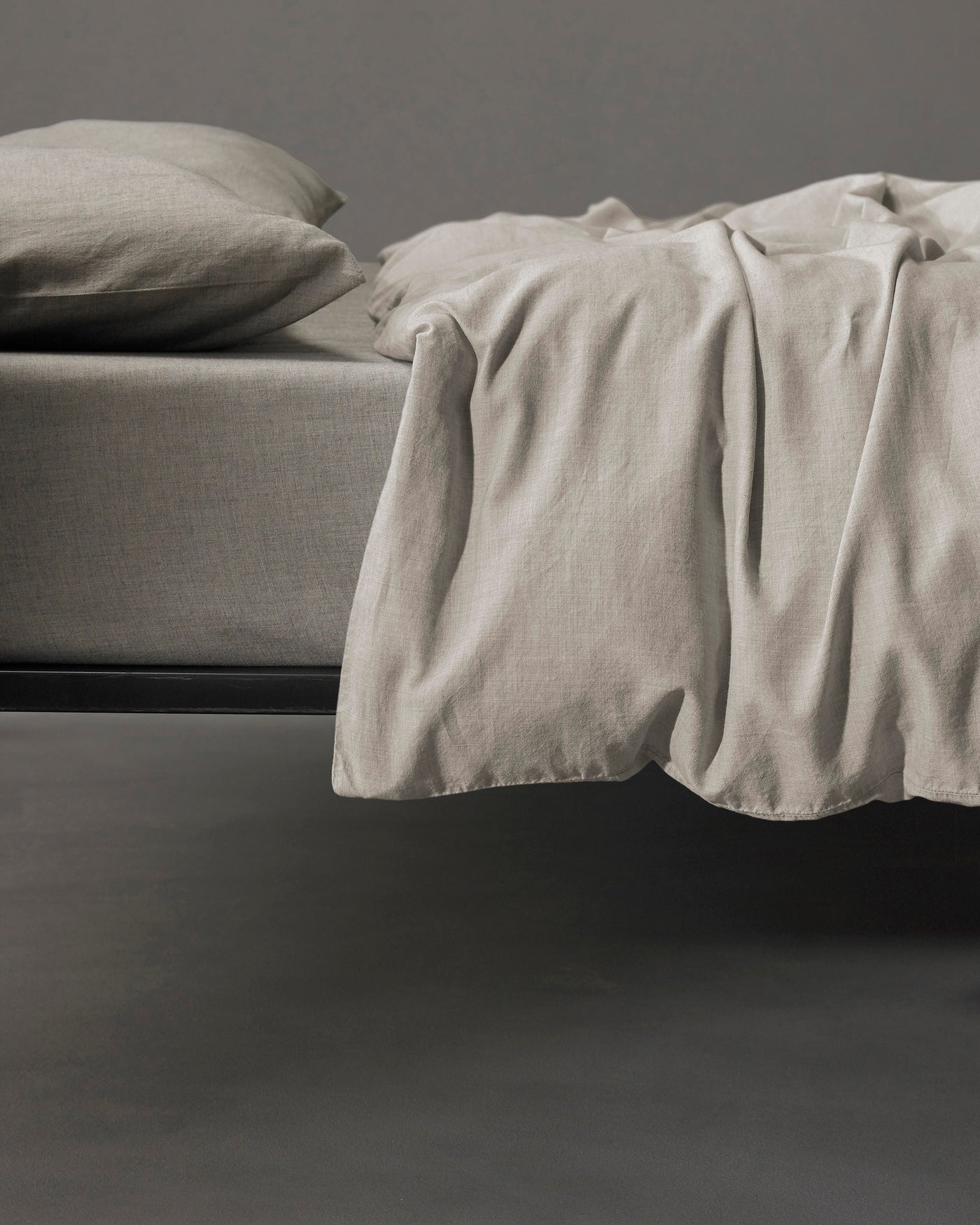 Society Limonta Smir duvet cover in stone linen, draped over a dark-framed bed.