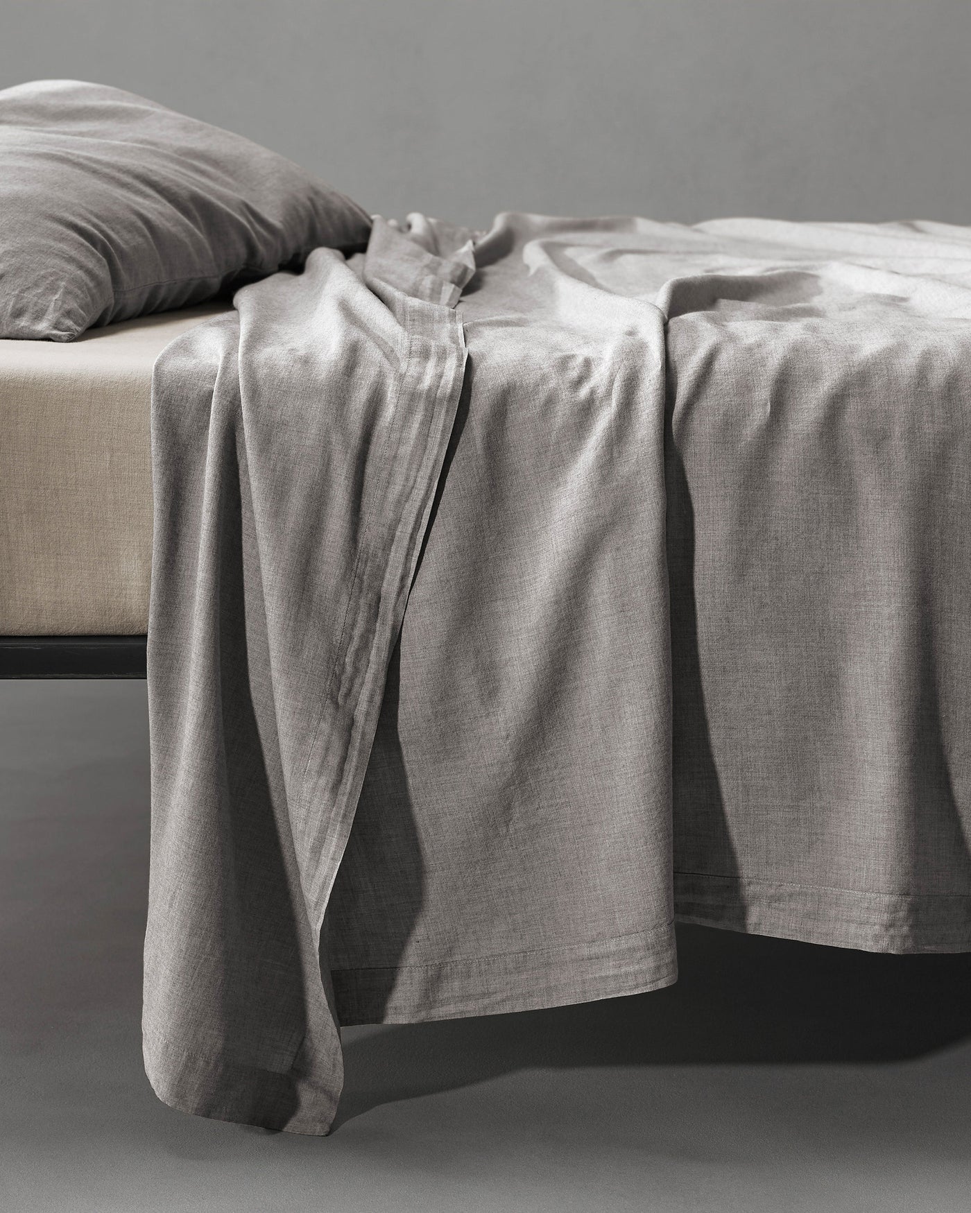Society Limonta Smir flat sheet in silver-grey linen draped loosely over bed edge.