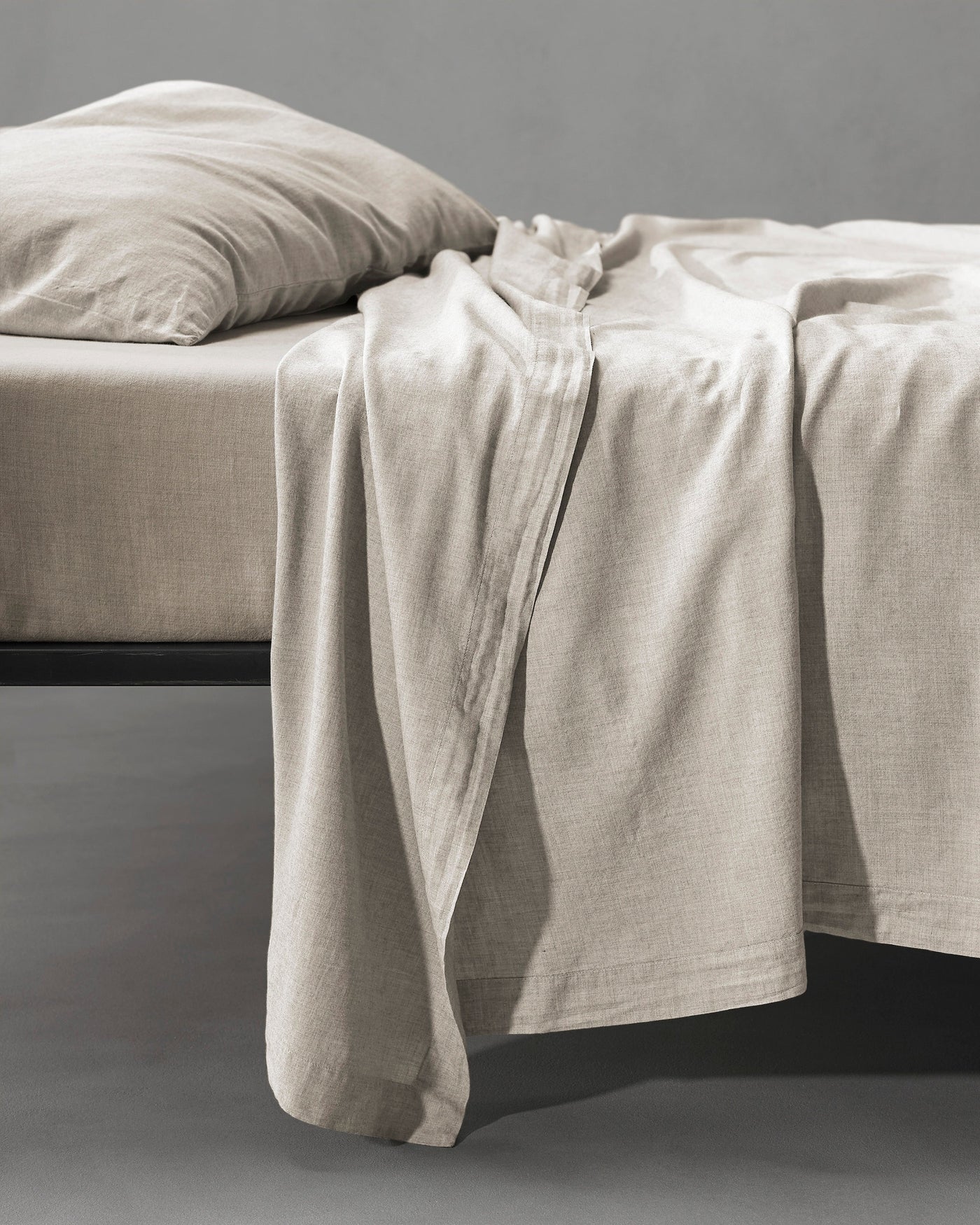 Society Limonta Smir flat sheet in natural linen draped over a black bed frame.